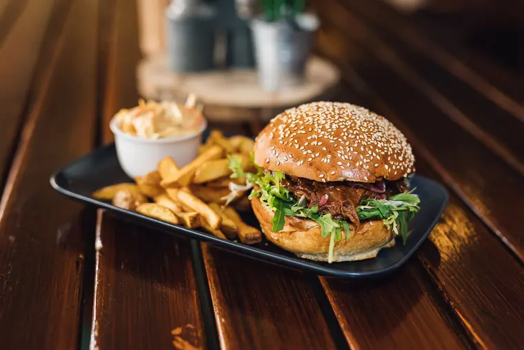 Burger v sezamové housce s hranolky na černém tácu